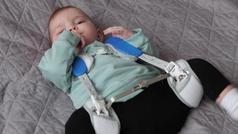 close up of baby girl in pavlik harness to correct hip dysplasia on blanket