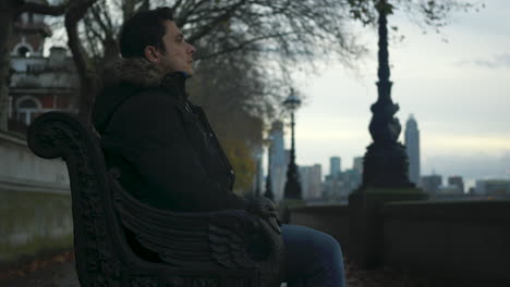 young man sits alone on a park bench and looks at the city slider shot