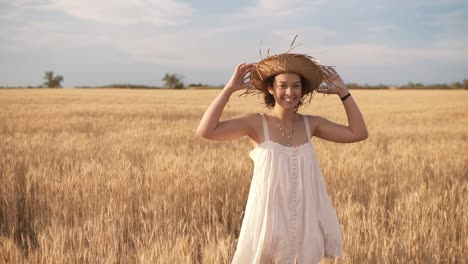 beautiful brunette curly lady in wheat field at summer. smiling and posing in straw hat. front view