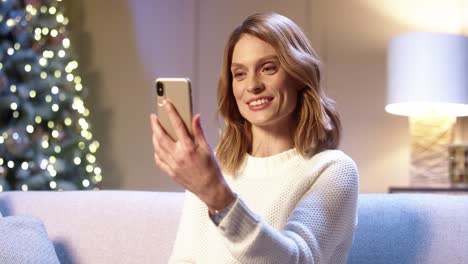 close up portrait of joyful woman speaking on video call online on smartphone receiving holidays greetings on christmas eve while sitting in cozy room near glowing xmas tree new year concept