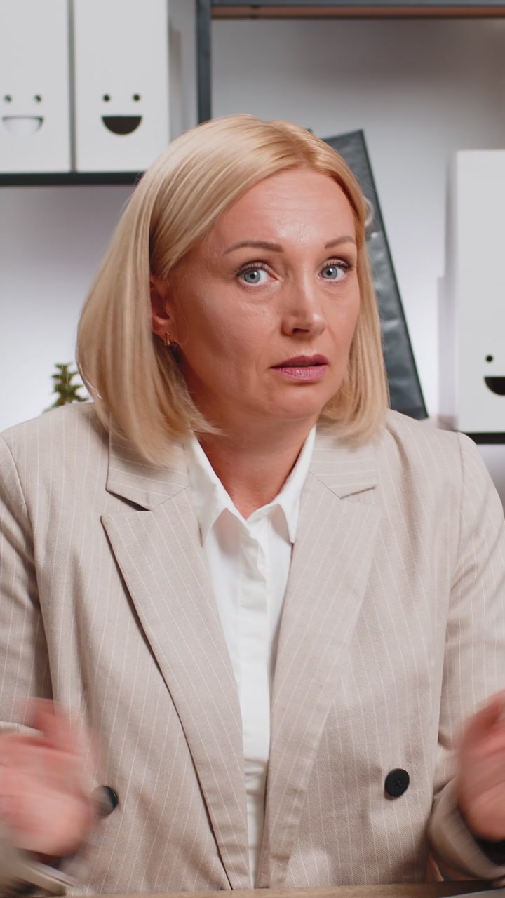 Confusa donna d'affari matura che fa gesti senza idea mentre è seduta con il portatile alla scrivania dell'ufficio di casa