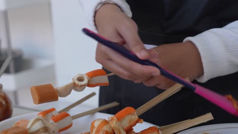 Young-Woman-In-Apron-Making-Suki-Satay-And-Spreading-Chili-Sauce-On-Each-Skewers