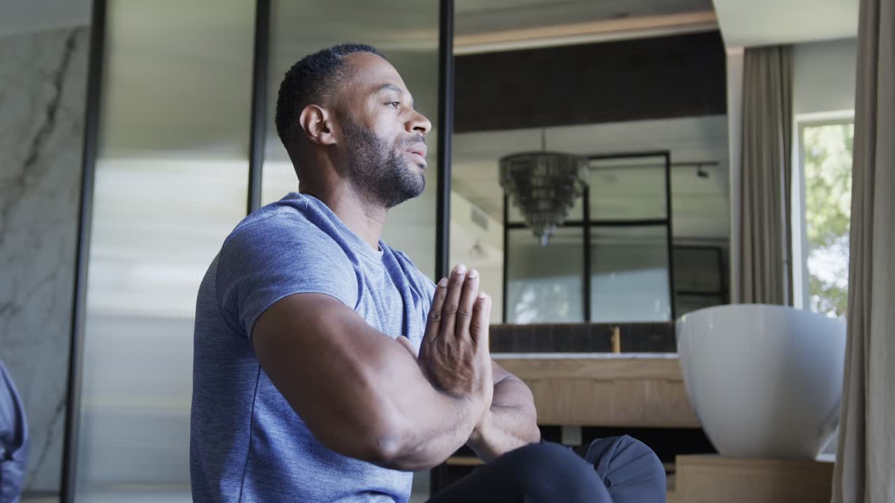 African American man sitting prayer pose opening eyes to sunlight at home with planter, copy space