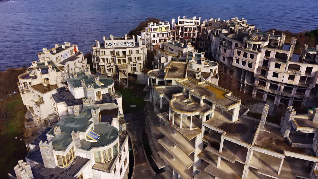 Esplora la bellezza spettrale degli edifici costieri abbandonati, immersi nelle acque serene della baia, che riflettono un fascino inquietante nella luce morente del crepuscolo.