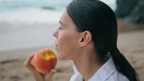 Mujer-Soñadora-Degustando-Melocotón-Sentado-En-La-Playa-De-Arena-En-Vacaciones-Cerca-Vertical