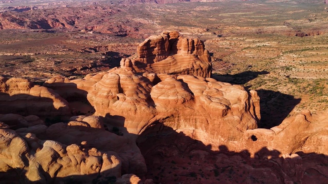 Splendido filmato stock del Parco Nazionale di Arches, USA, durante un pomeriggio luminoso. La luce solare brillante illumina le maestose strutture di arenaria rossa e il paesaggio desertico sotto un cielo azzurro limpido.