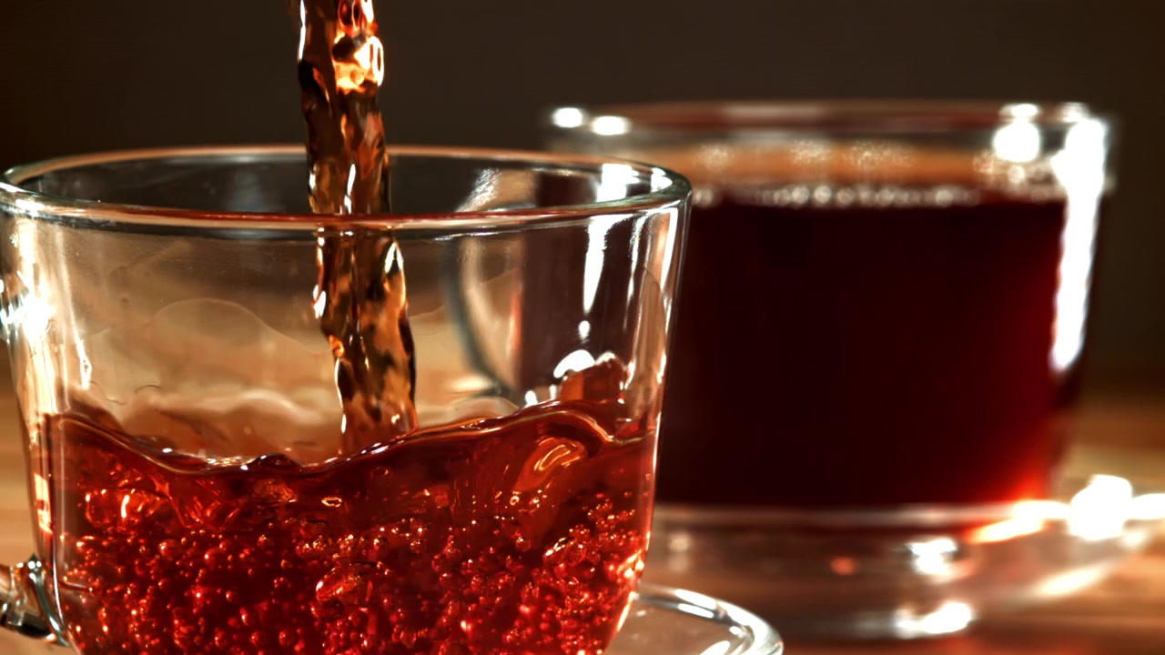 Versamento al rallentatore di tè rosso scuro in una tazza di vetro