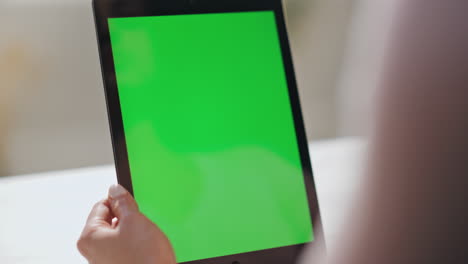 las manos de la mujer deslizando la tableta de pantalla verde viendo las redes sociales en casa de cerca.
