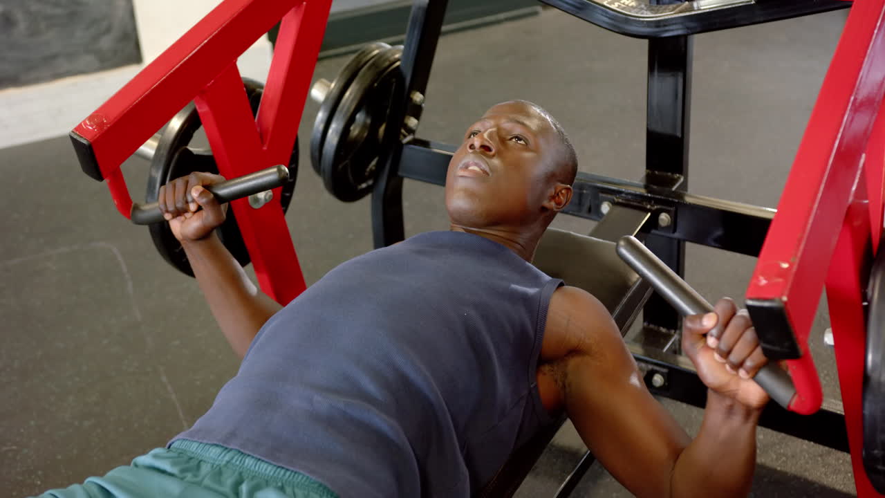 Lifting weights on bench press, african american man focusing on strength training in gym