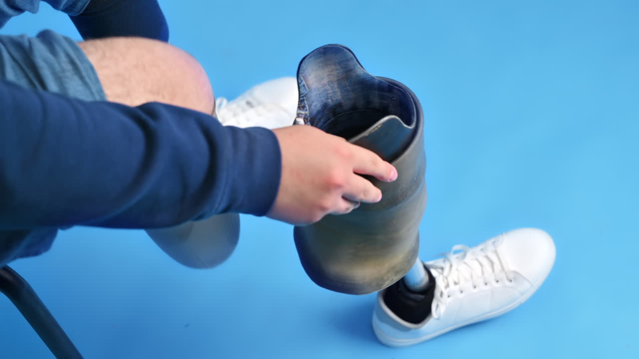 View of a man with prosthetic legs and white sneakers. Removing the prosthesis while sitting on a chair, blue background