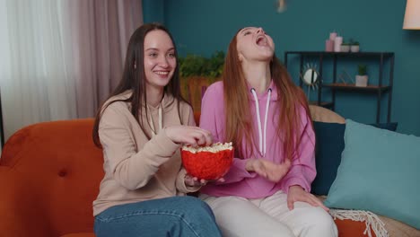 girls friends siblings watching favorite tv show movie and eating popcorn, sitting on sofa at home