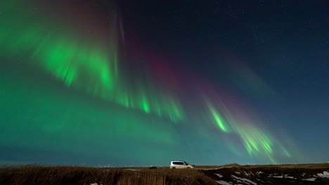 Time-lapse-shot-of-flickering-green-and-purple-aurora-borealis-at-night-sky-of-Iceland-with-parking-car-on-road---wide-shot