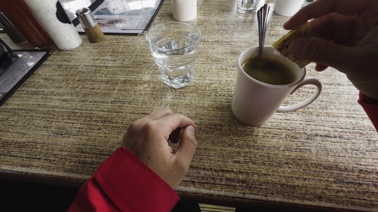 A comforting, cozy first-person view of a traveler resting at a diner table. mindfully adding brown sugar to a cup , enjoying a completely calm, peaceful moment of solitude to warm right up alone