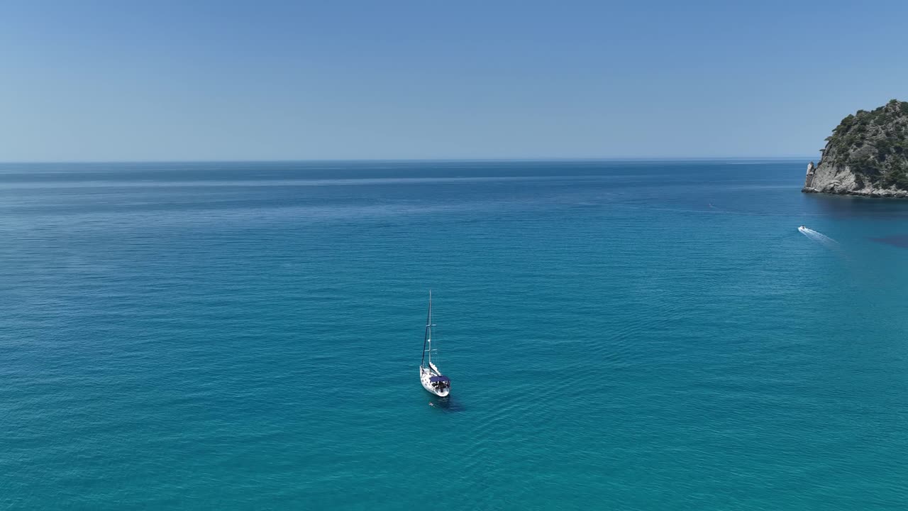 un velero navegando por las aguas turquesas cerca de la costa rocosa de la isla de corfú, grecia, bajo un cielo azul claro