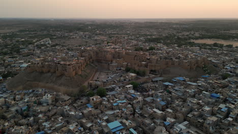 an evening orbit drone view of jaisalmer fort, rajasthan, india, surrounded by sandstone houses. the fort glows golden under a vibrant sky with hues 4k