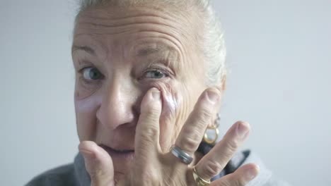 senior caucasian lady with white her applies herself white cream make up closeup shot looking at camera, face portrait