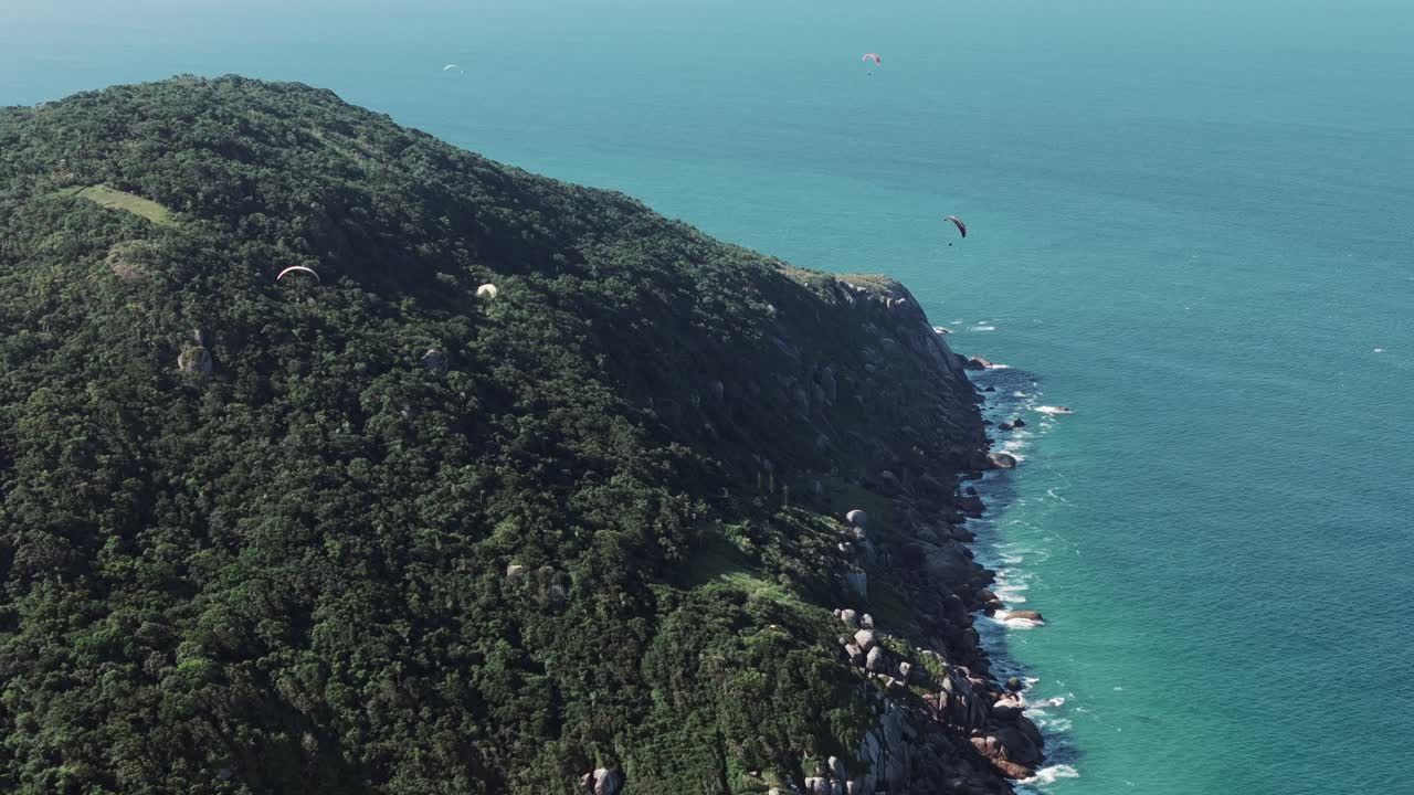 Florianopolis'teki Praia Brava'da dağlık arazi boyunca zarifçe süzülen çok sayıda yamaç paraşütçüsü