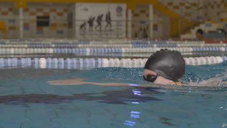 close up lateral tracking shot of a young female swimmer swimming breaststroke actively in indoor pool