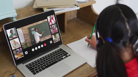 Girl-doing-homework-and-having-a-video-conference-with-teacher-and-classmates-on-laptop-at-home