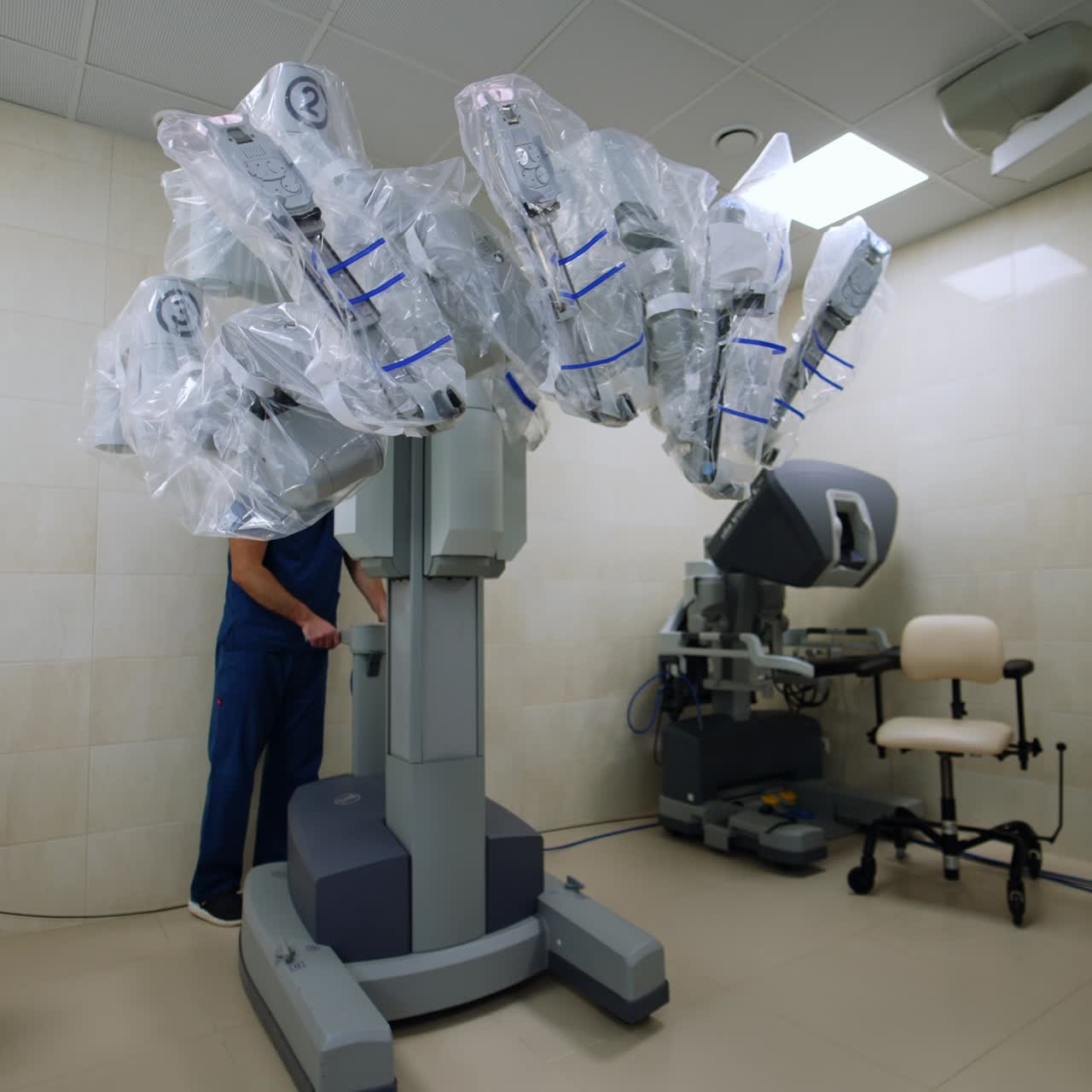 Medic in dark blue uniform stands behind the Da Vinci robot. Specialist moves the equipment closer to a patient