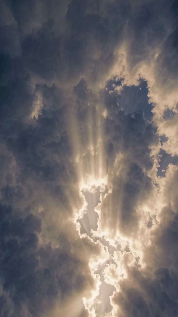 Dramatic upward angle captures sun rays piercing through dark clouds, creating a cinematic