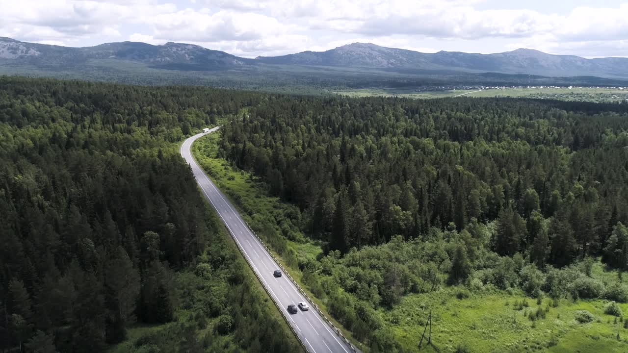 una vista aérea de un camino sinuoso a través de un bosque exuberante, con montañas en el fondo.