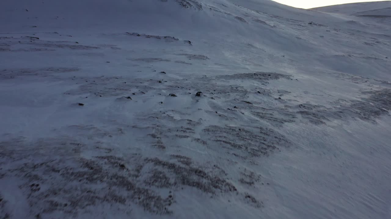 Revealing aerial shot of a snow covered hill and plains during strong winds.