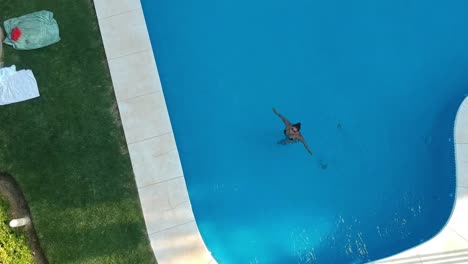 aerial drone view of a swimming pool with a girl in its clear water