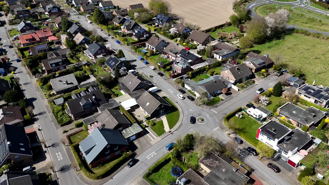 White and black car on roundabout of american city at spring day. Aerial top down flyover. solar panels on roof of single family house near agricultural farm fields. Quiet community in USA.