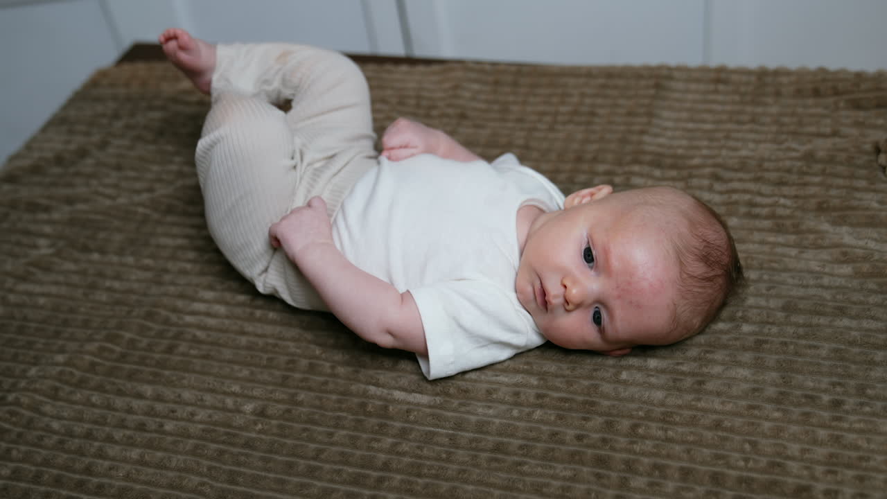 Two months old baby boy in white t-shirt and beige pants. Little child lies on the plaid and mom touches him tenderly.