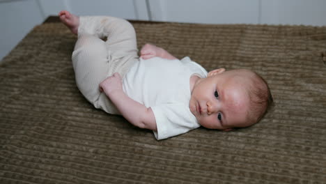 two months old baby boy in white t-shirt and beige pants. little child lies on the plaid and mom touches him tenderly.
