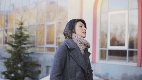 Woman-in-autumn-coat-walking-in-the-street-and-talking-with-someone