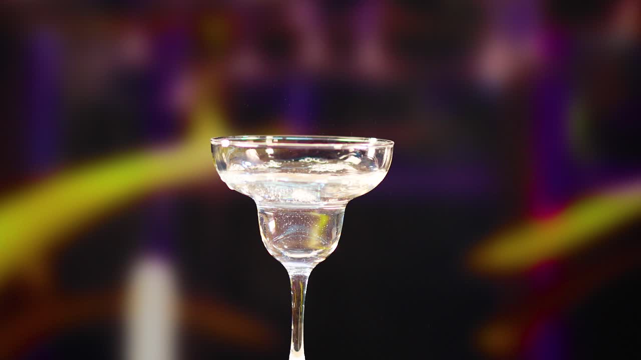 A martini glass is filled and garnished with a lemon twist against a vibrant, blurred background