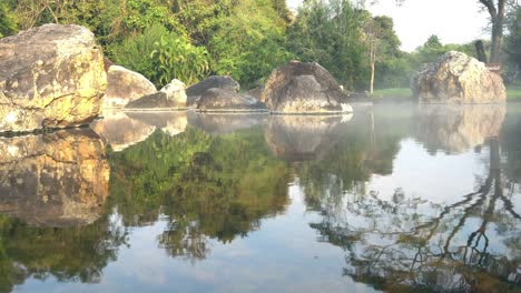 4k panorámica de izquierda a derecha de aguas termales naturales en la piscina de rocas bajo la luz del sol, el vapor flotando hacia arriba y la sombra de reflexión del árbol. parque nacional chaeson, lampang, tailandia.