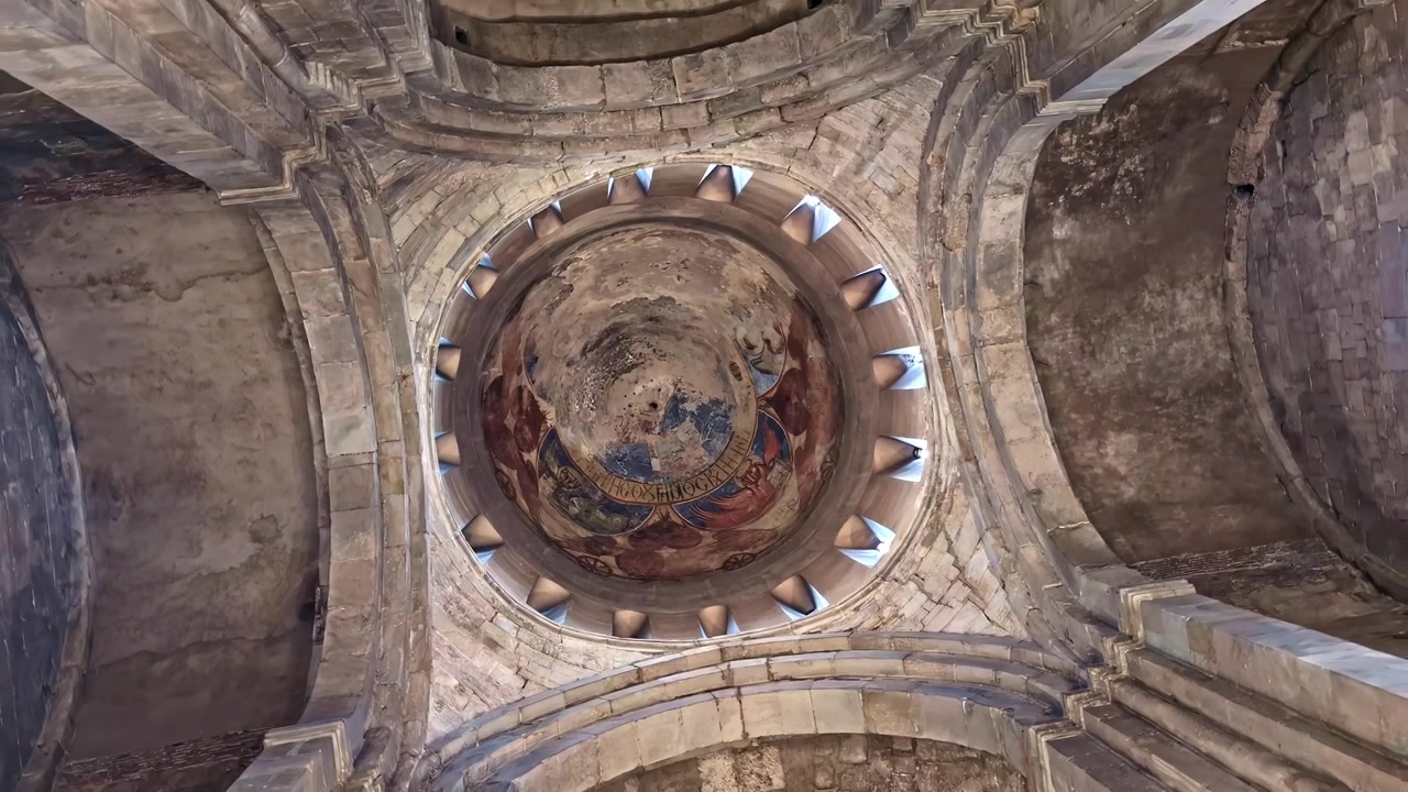 Vista verso l'alto dell'antica cupola di una cattedrale con affreschi religiosi sbiaditi e archi in pietra