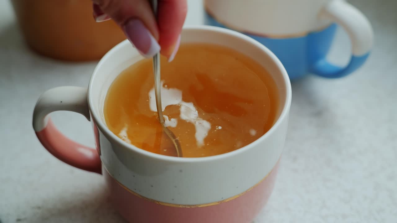 Herbal infusion swirl with honey in cozy ceramic mugs on windowsill, Slow motion