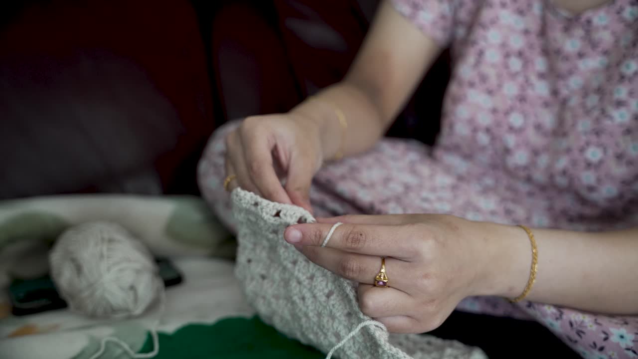 Woman sitting comfortably on a sofa, crocheting with white thread, enjoying a relaxing pastime and expressing her creative skills