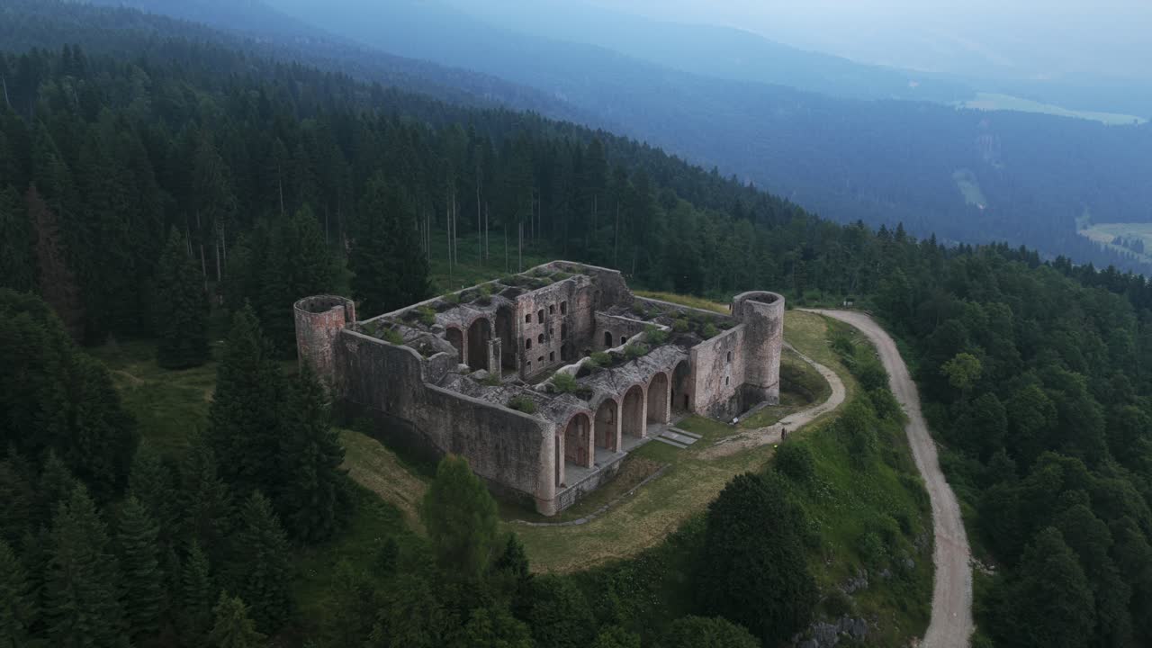Aerial view of historic Forte Interrotto ruins on hilltop. Overgrown fortress surrounded by foggy pine forest. For travel or history content, Asiago, Italy