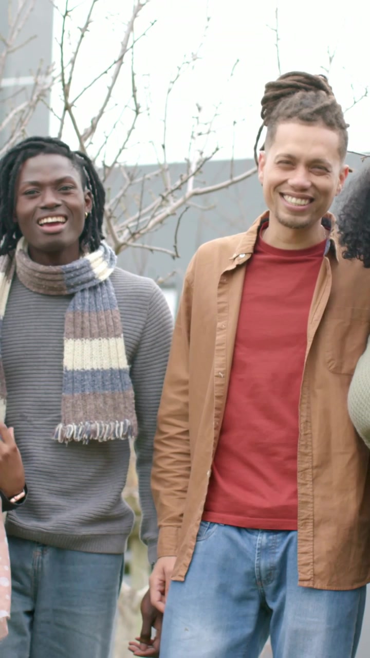 Vertikal video: Talende gruppe deler joke, hovedmanden gestikulerer, mens andre griner i gården, tørklæde.