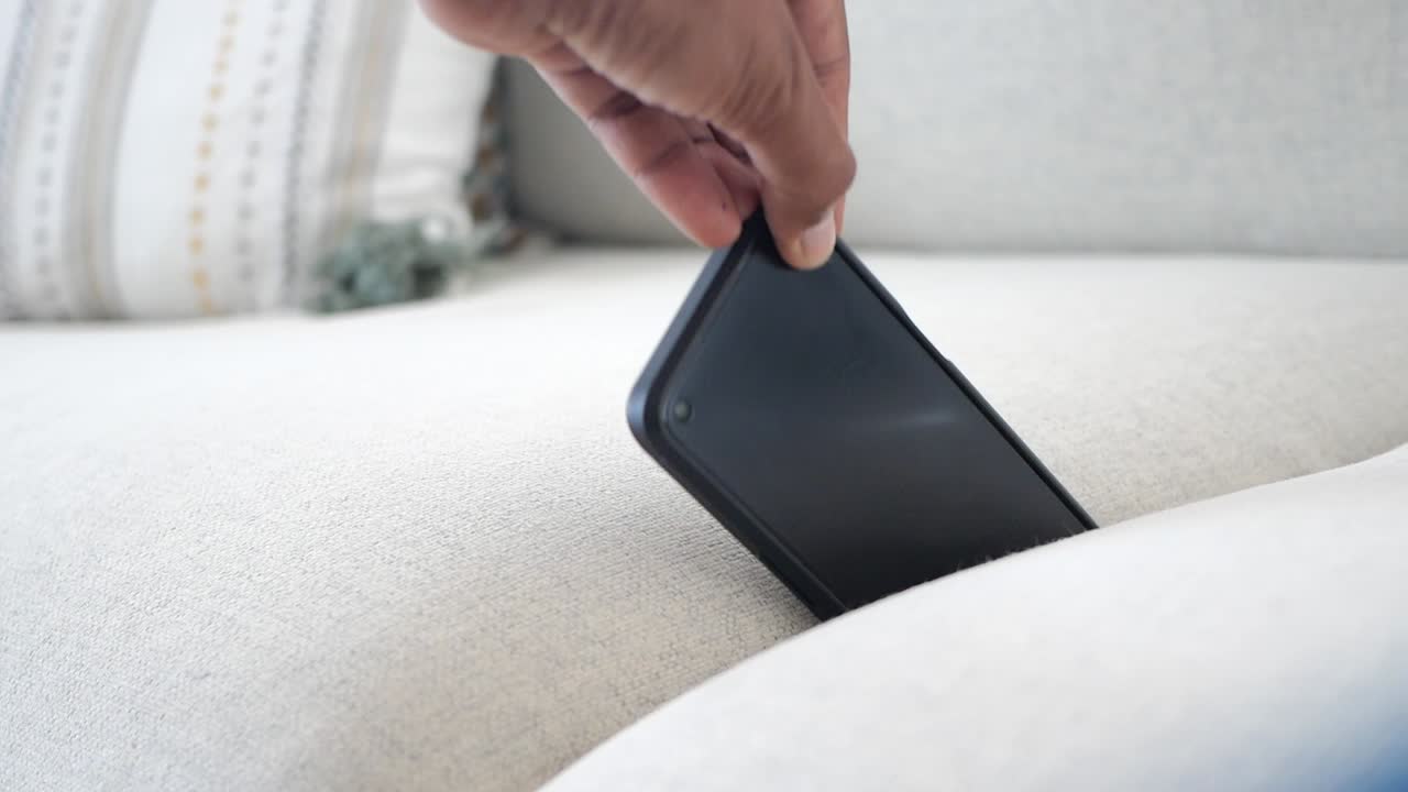 Hand reaching for a smartphone on a couch