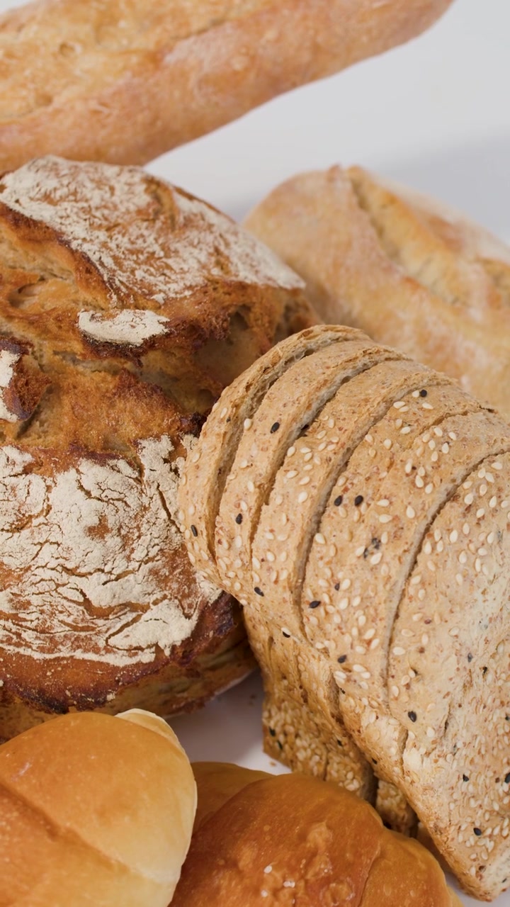 Primo piano dall'alto di pane a lievitazione naturale, baguette e croissant che ruotano sotto una luminosa illuminazione da studio.