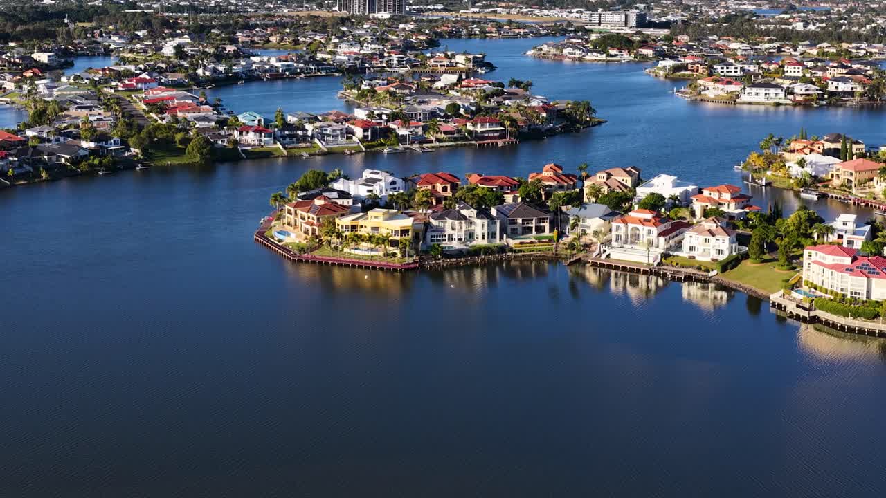 Drone footage glides over upscale waterfront houses and winding river in Gold Coast, Australia, under bright daylight with smooth, steady camera movement