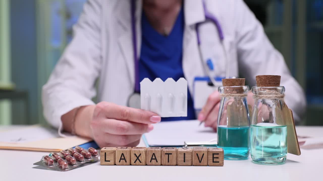 Doctor holding medication with "LAXATIVE" blocks on table