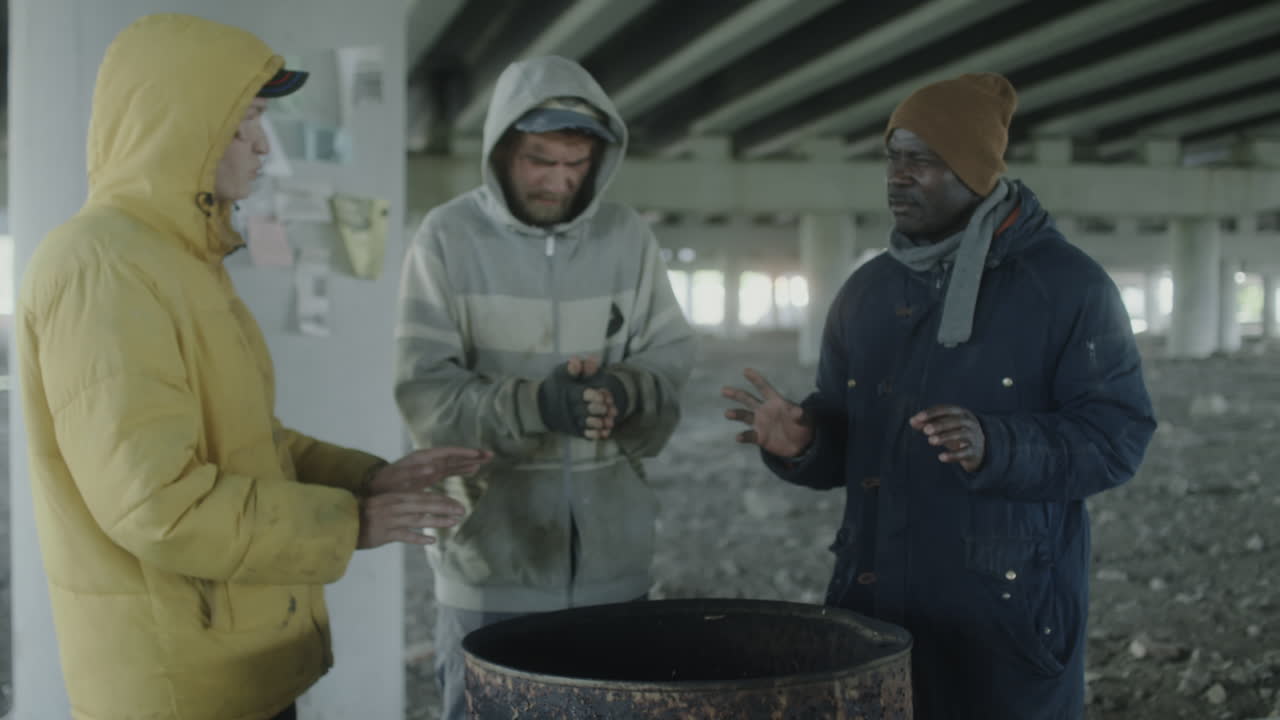 Three Homeless Men Huddling for Warmth Around a Barrel Under an Overpass