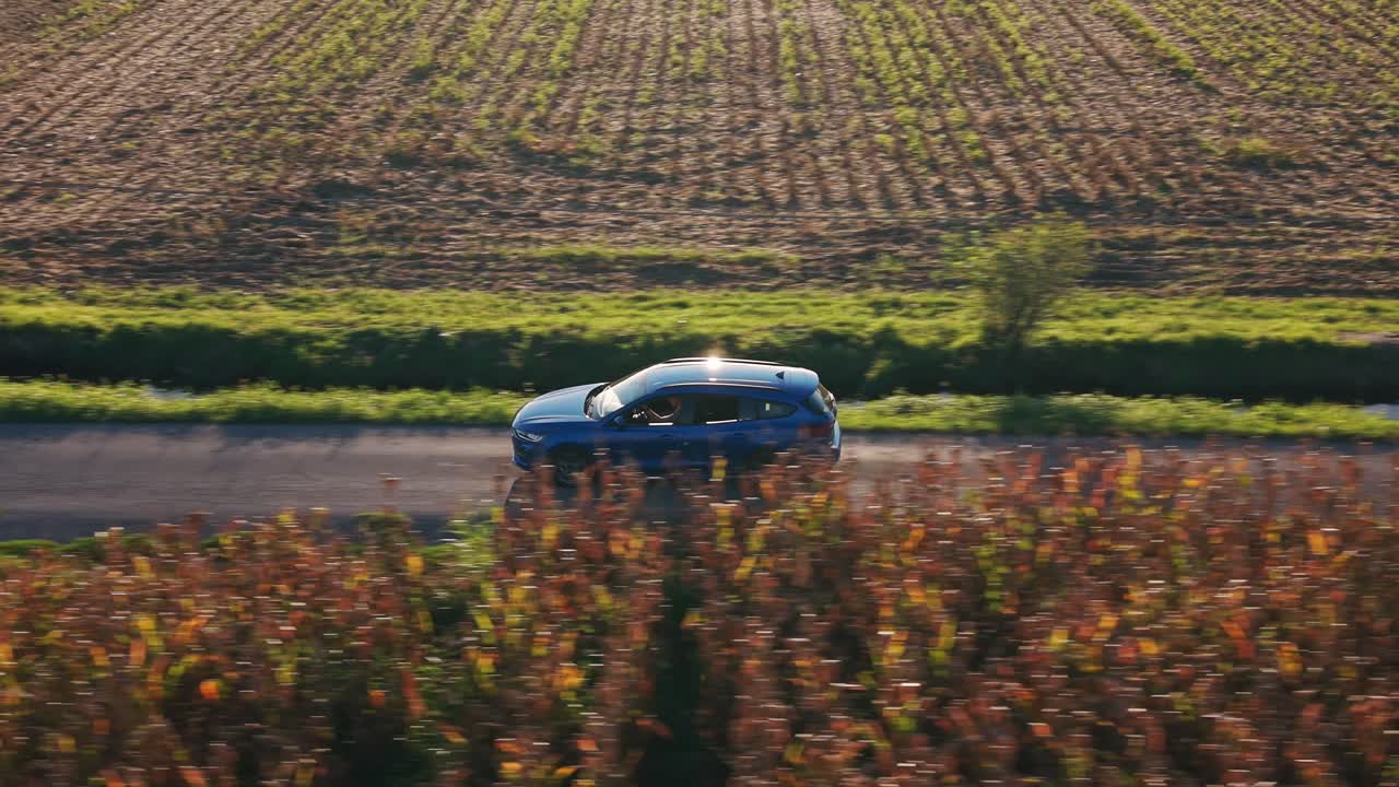 Auto blu che percorre una strada di campagna tra campi coltivati al tramonto a Soncino, Italia.