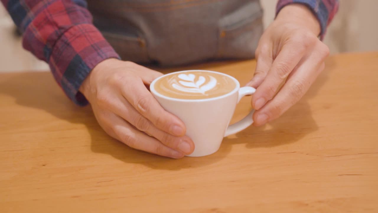 Barista puts down to counter cup of cappuccino with latte art