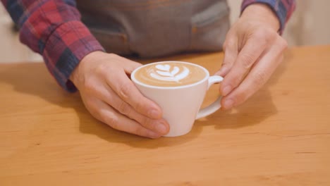 el barista pone en el mostrador una taza de capuchino con arte latte.