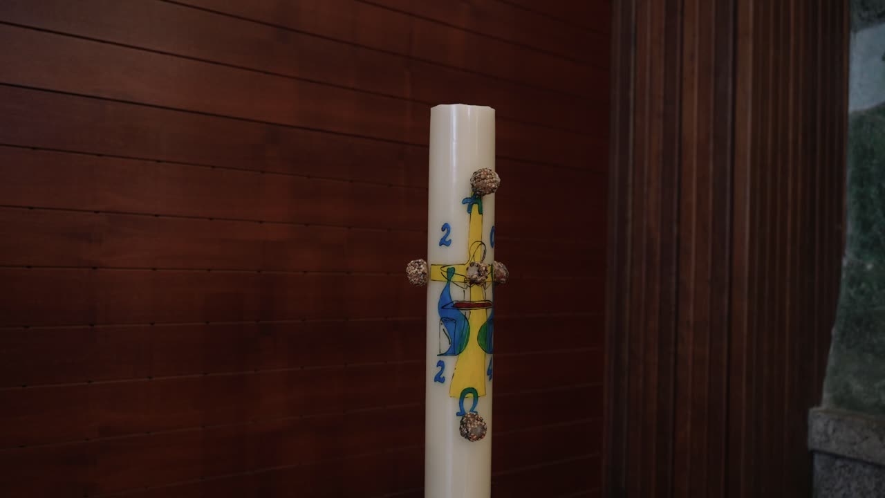 Tall Paschal candle with Alpha Omega symbols inside church against wooden wall