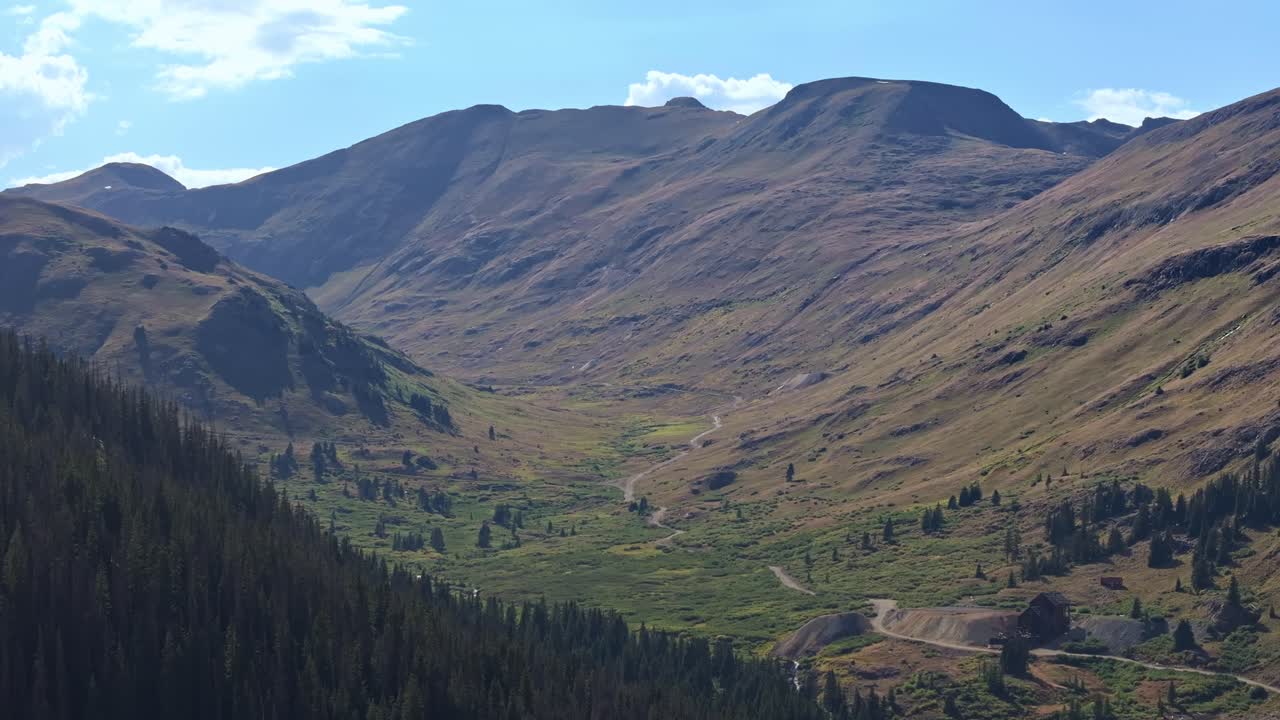Dolci colline e valli alpine sotto un cielo estivo sereno, ripresa aerea che si sposta a destra.