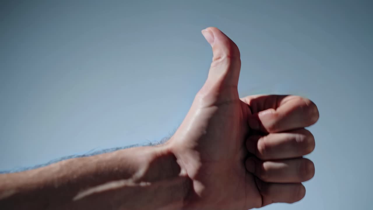 Close-up of a hand giving a thumbs-up against a clear sky, captured from a low angle